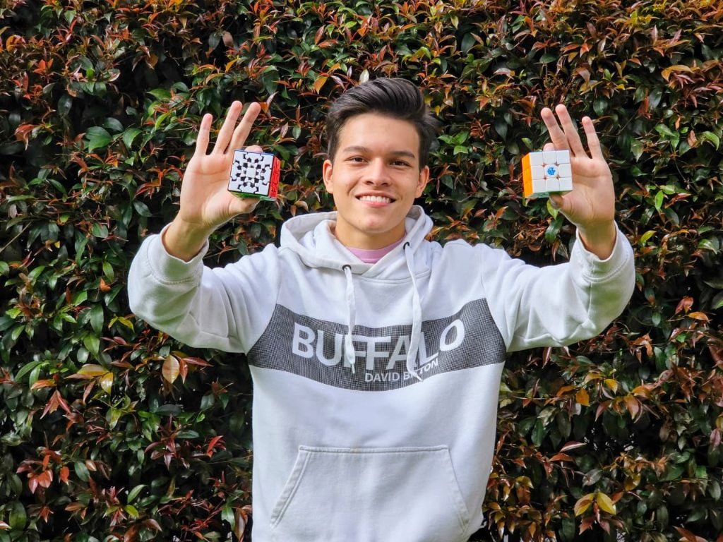 Coach Joseph Jimenez smiling and holding two twisty puzzles outdoors