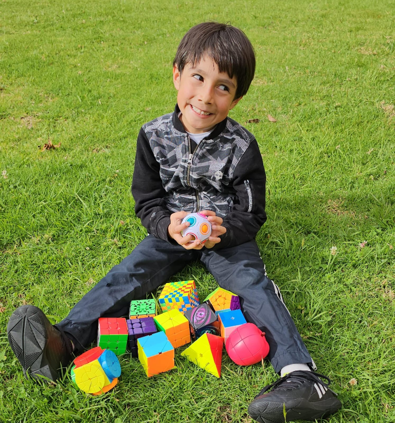 Joseph’s brother sitting on the grass among his collection of twisty puzzles